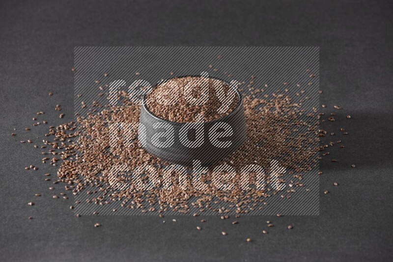 وعاء فخاري أسود ممتلئ بحبوب بذر الكتان محاط بالبذور على أرضية سوداء