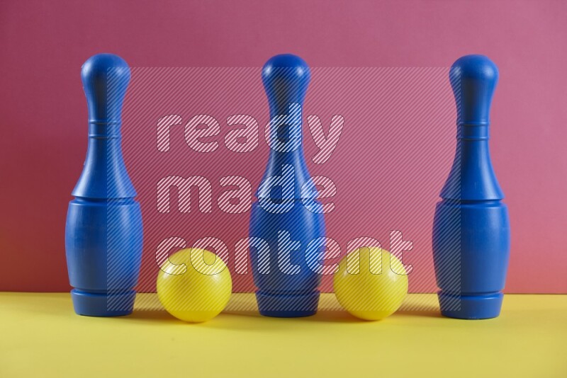 Plastic bowling pins with balls on pink and yellow background (kids toys)