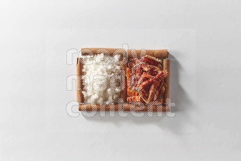 2 squares of cinnamon sticks full of dried red chilis and white salt on white flooring