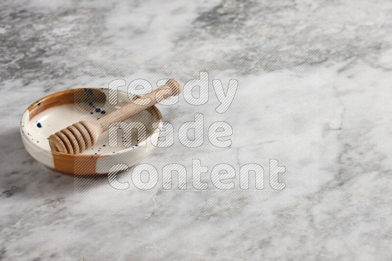 Multicolored pottery bowl with wooden honey dipper in it on grey marble background