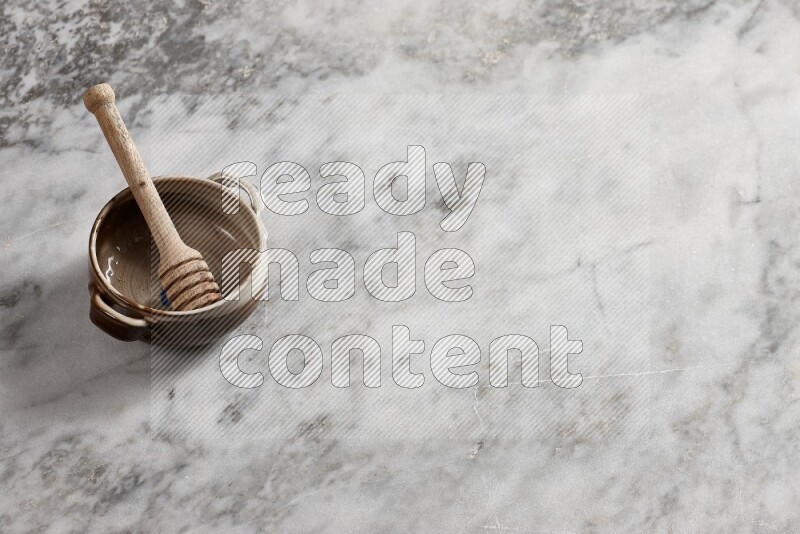 Multicolored pottery bowl with wooden honey dipper in it on grey marble background