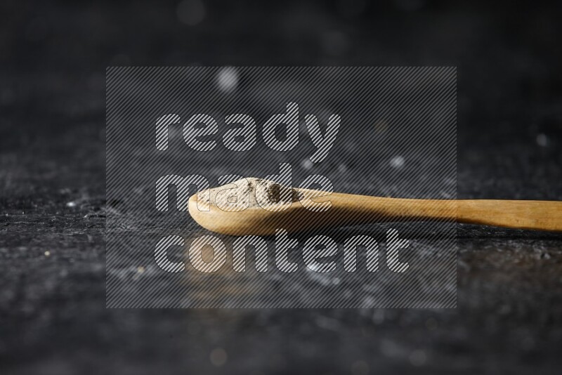 A wooden spoon full of white pepper powder on textured black flooring
