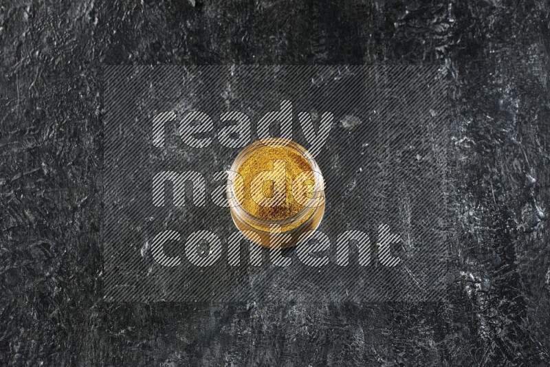 وعاء زجاجي ممتلئ ببودرة الكركم على خلفية سوداء