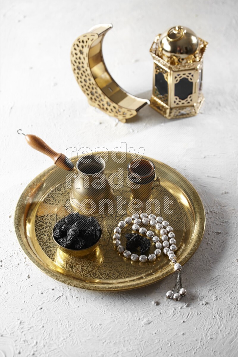 Dried plums in a metal bowl with coffee and prayer beads on a tray beside lanterns in a light setup