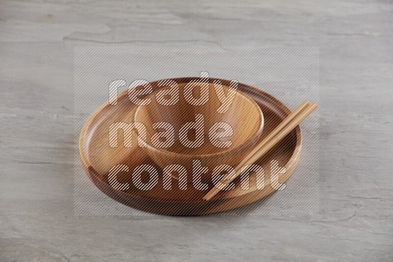 brown wood round bowl on top of brown wood round plate and wood chopsticks, on grey textured countertop