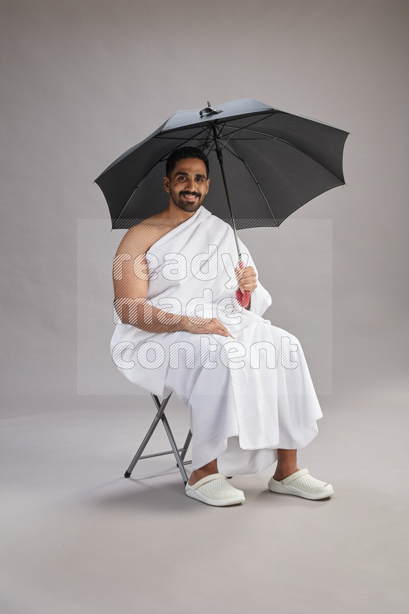 A man wearing Ehram with face mask Standing holding umbrella on gray background