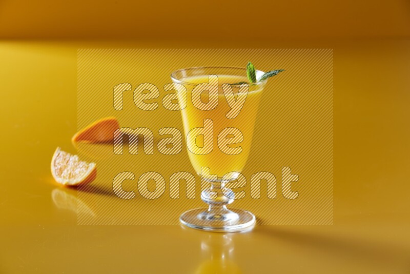 glass of orange juice with  mint on yellow background