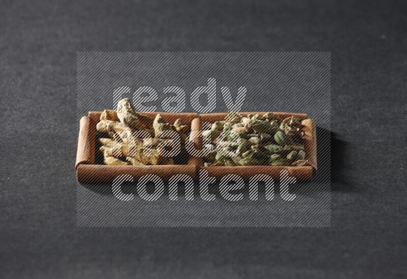 مربعان من أعواد القرفة ممتلئان بحبوب الهيل وأصابع الكركم علي خلفية سوداء