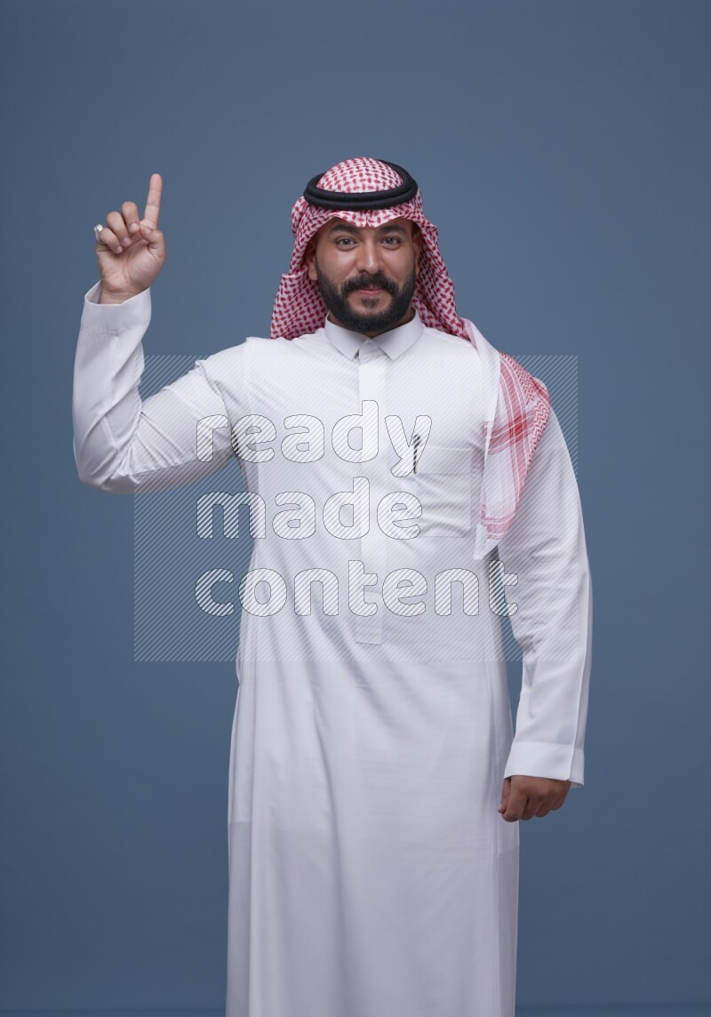 A man pointing on blue background wearing Saudi Thob with Shomag