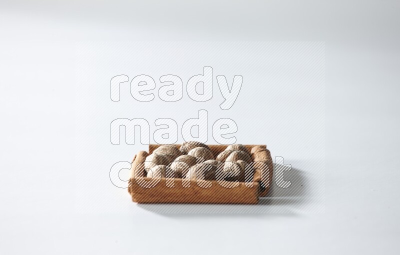 أربعة من أعواد القرفة مكونة شكل مربع بداخلها جوزة الطيب علي خلفية بيضاء