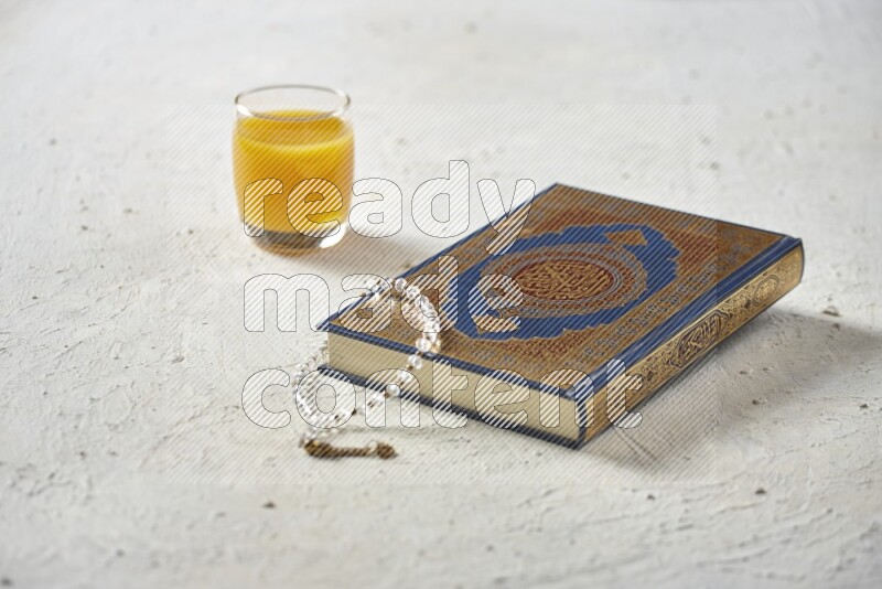Quran with dates, prayer beads and different drinks all placed on textured white background