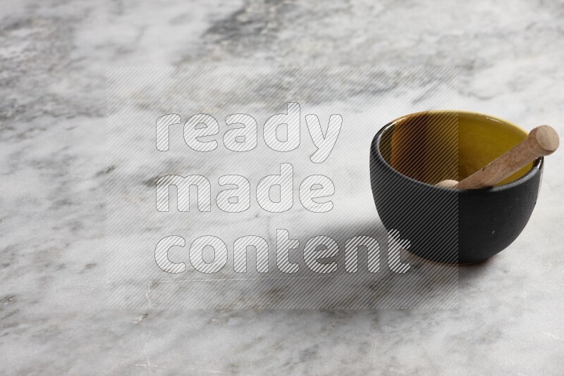 وعاء فخاري متعدد الألوان مع ملعقة عسل خشبية بداخله على خلفية من الرخام الرمادي