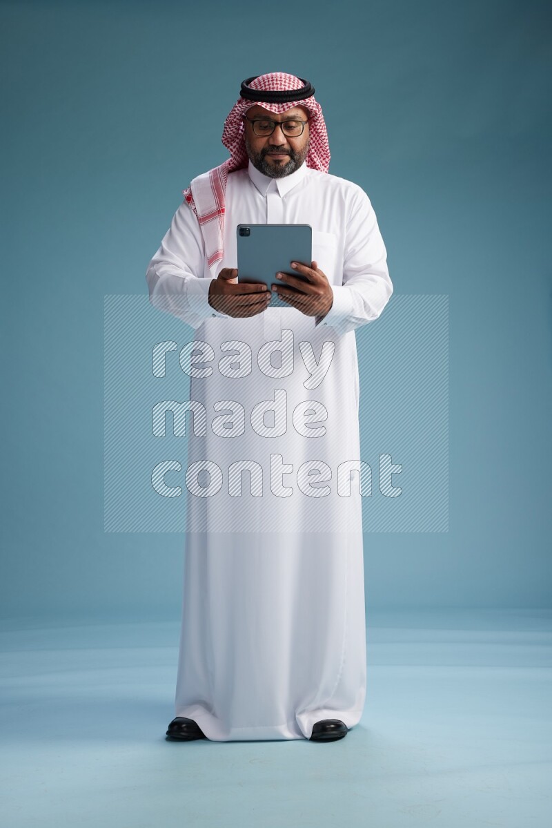 Saudi Man with shimag Standing holding a tablet on blue background