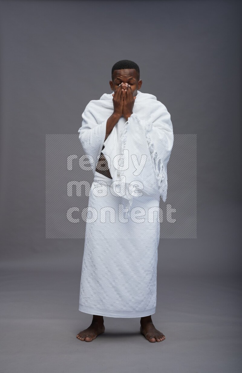 A man wearing Ehram standing showing how to sneeze on gray background