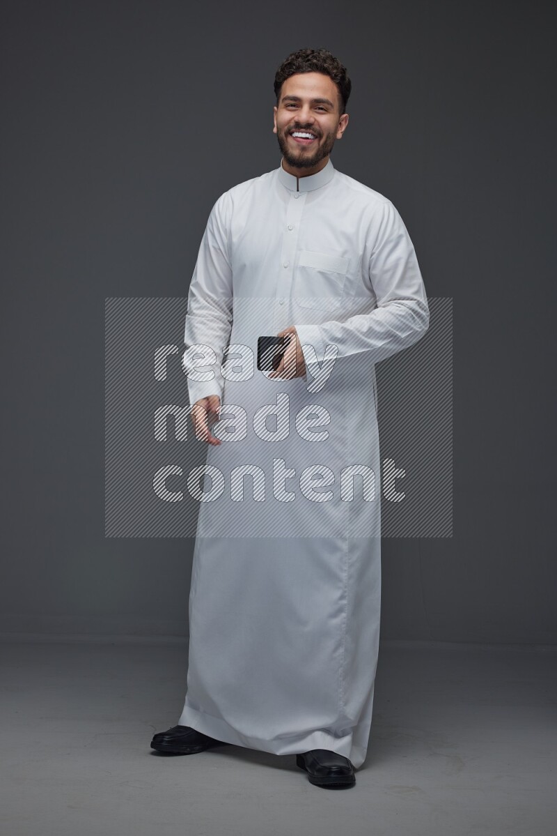 A Saudi man wearing Thobe and taking selfie with his phone making different poses eye level on a gray background