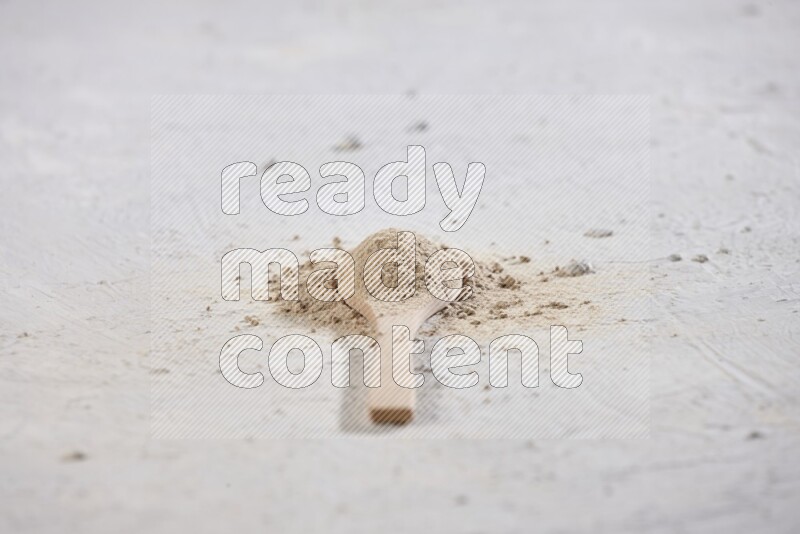 ملعقة خشبية مليئة ببودرة الثوم مع بعض بودرة الثوم المتناثرة حولها على خلفية بيضاء