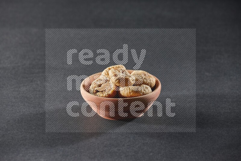 A wooden bowl full of dried figs on a black background in different angles