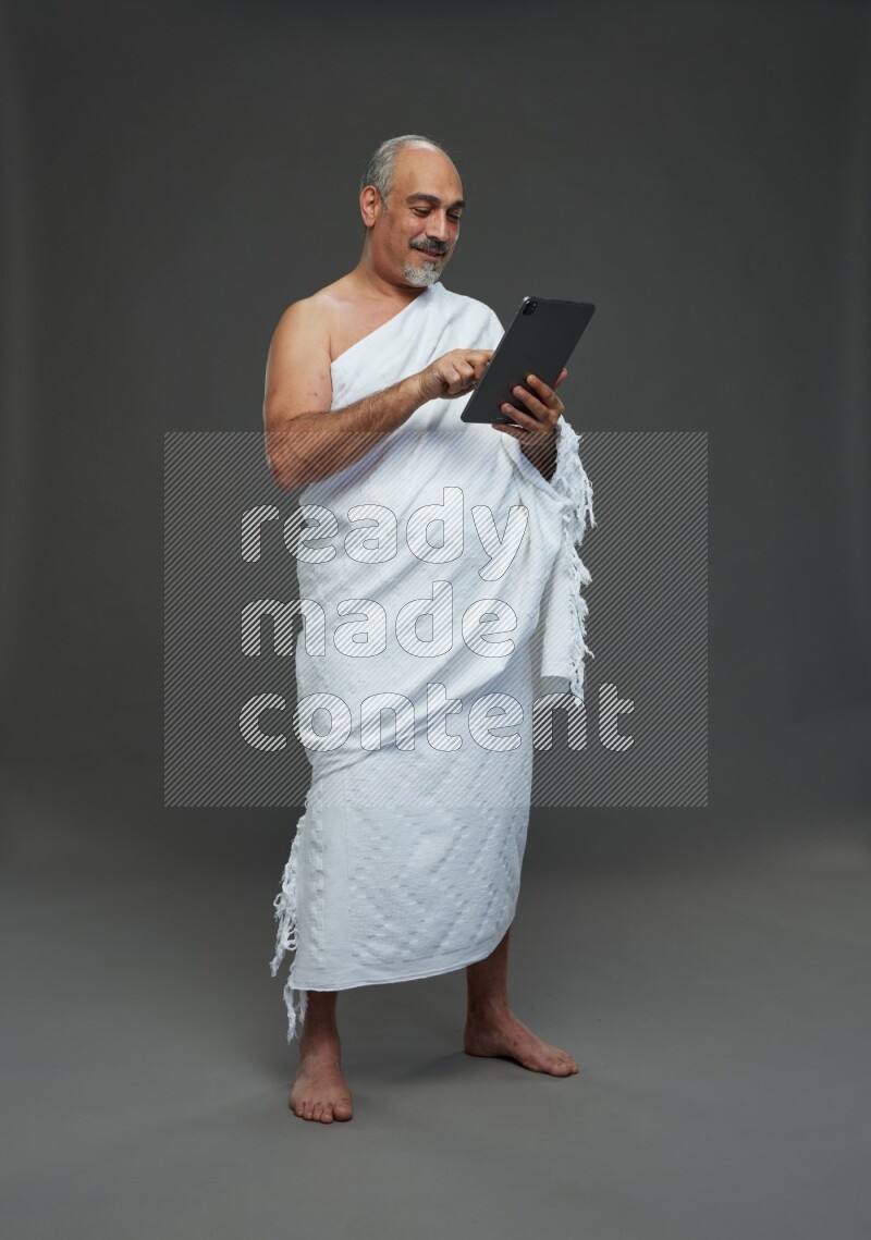 A man wearing Ehram Standing working on tablet on gray background