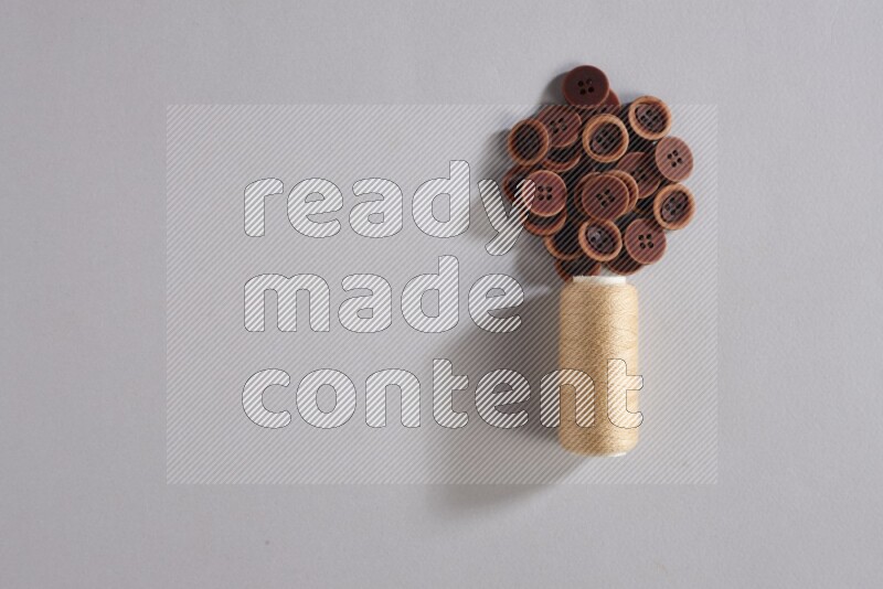 بكرة خيط خياطة بيج مع مجموعة صغيرة من الأزرار على خلفية رمادية