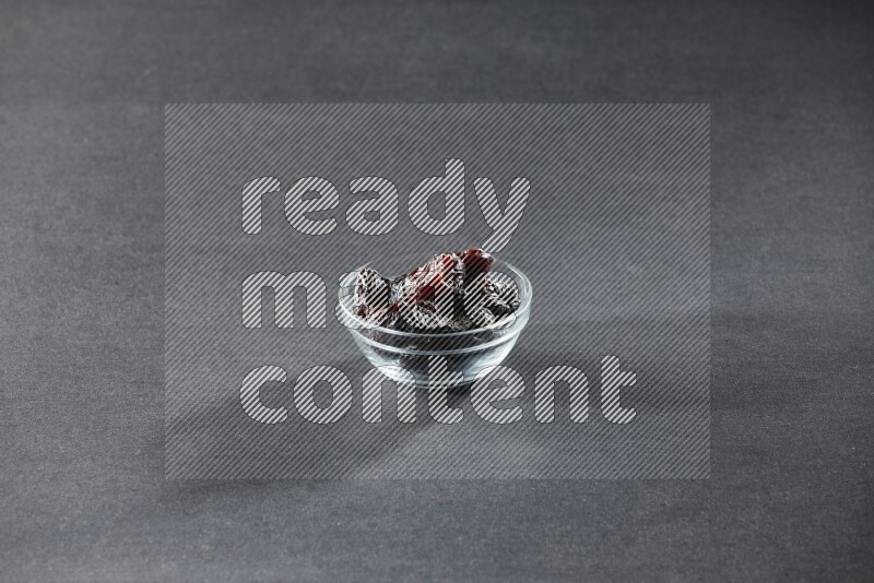 A glass bowl full of dried plums on a black background in different angles