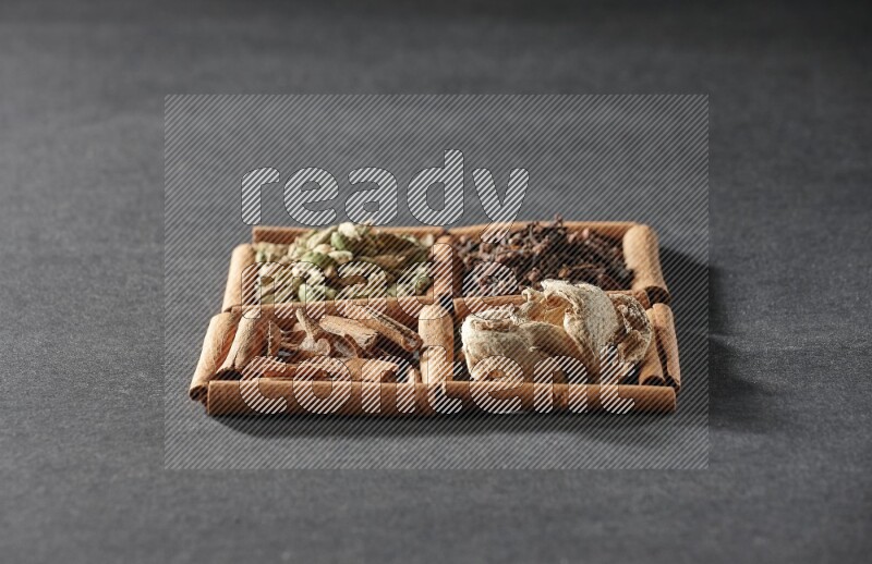 4 مربعات من عيدان القرفة ممتلئة بقطع القرفة وحبوب الهيل والقرنفل والزنجبيل المجفف على أرضية سوداء