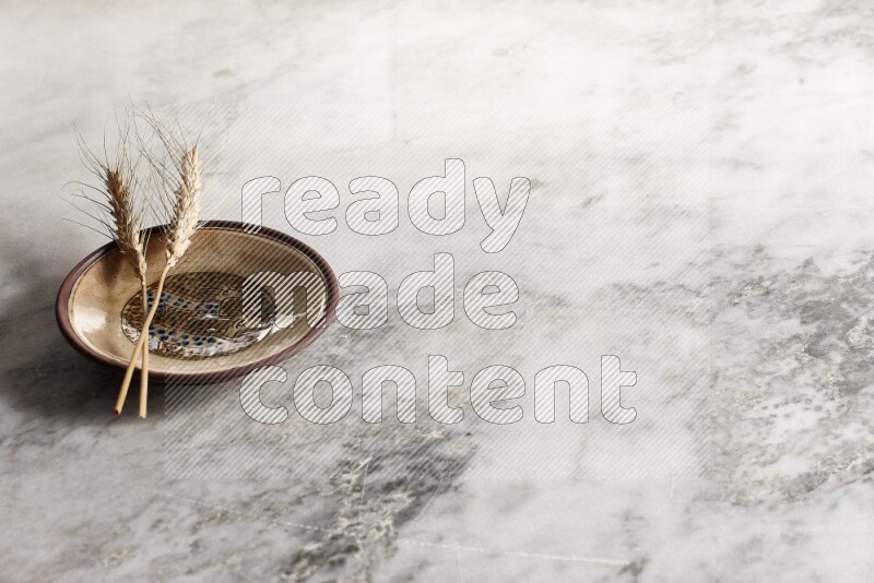 Wheat stalks on decorative pottery plate on grey marble background