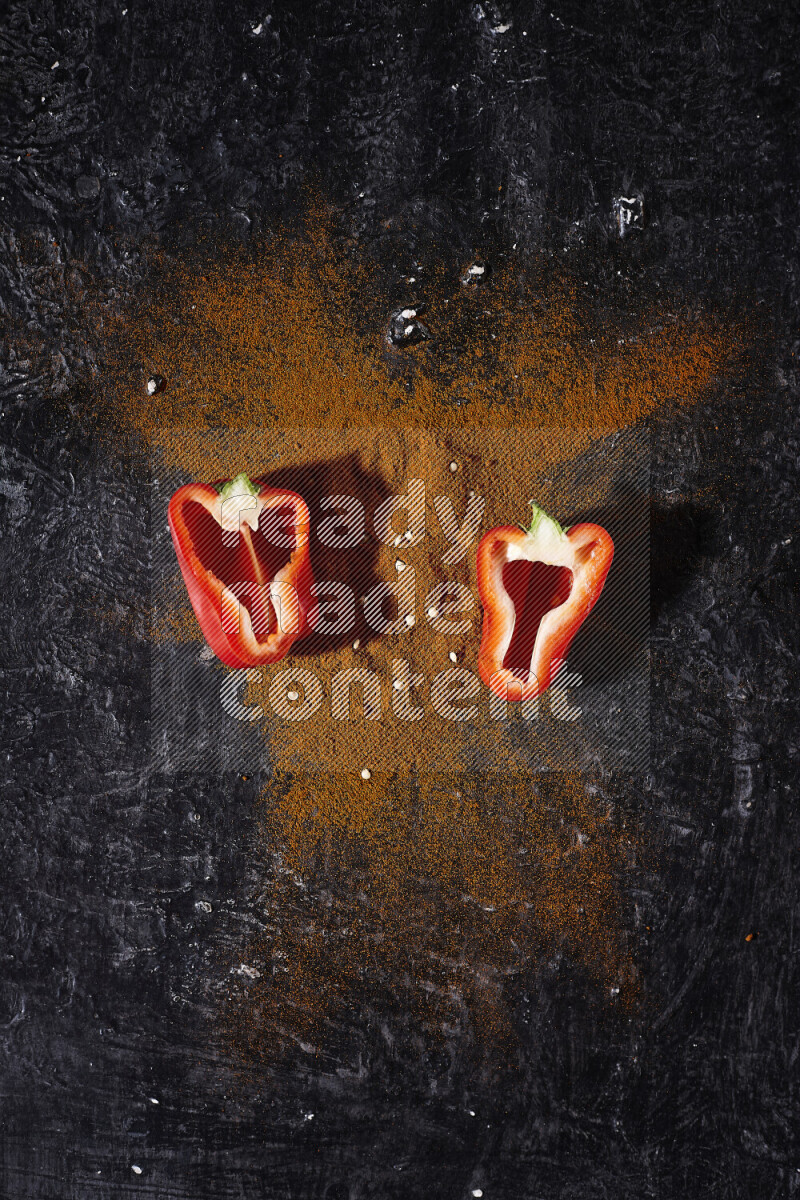 A bunch of ground paprika powder with two halfs of red bell pepper on black background