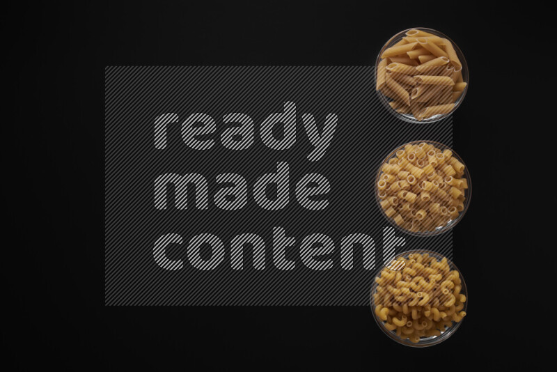 Different pasta types in 3 glass bowls on black background
