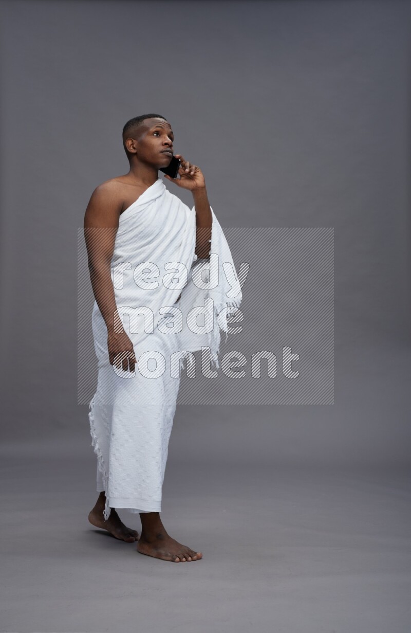 A man wearing Ehram Standing talking on phone on gray background