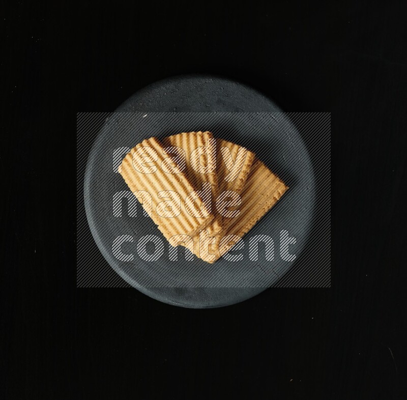 Golden biscuits in a black pottery plate on black background