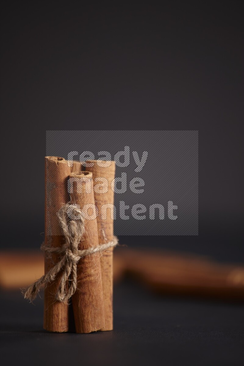 4 Cinnamon sticks stacked and bounded with more sticks in the background on black flooring