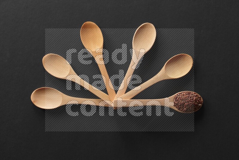 wooden spoons filled with white peppers, mustard seeds, black seeds, garden cress, cumin and flax on black flooring