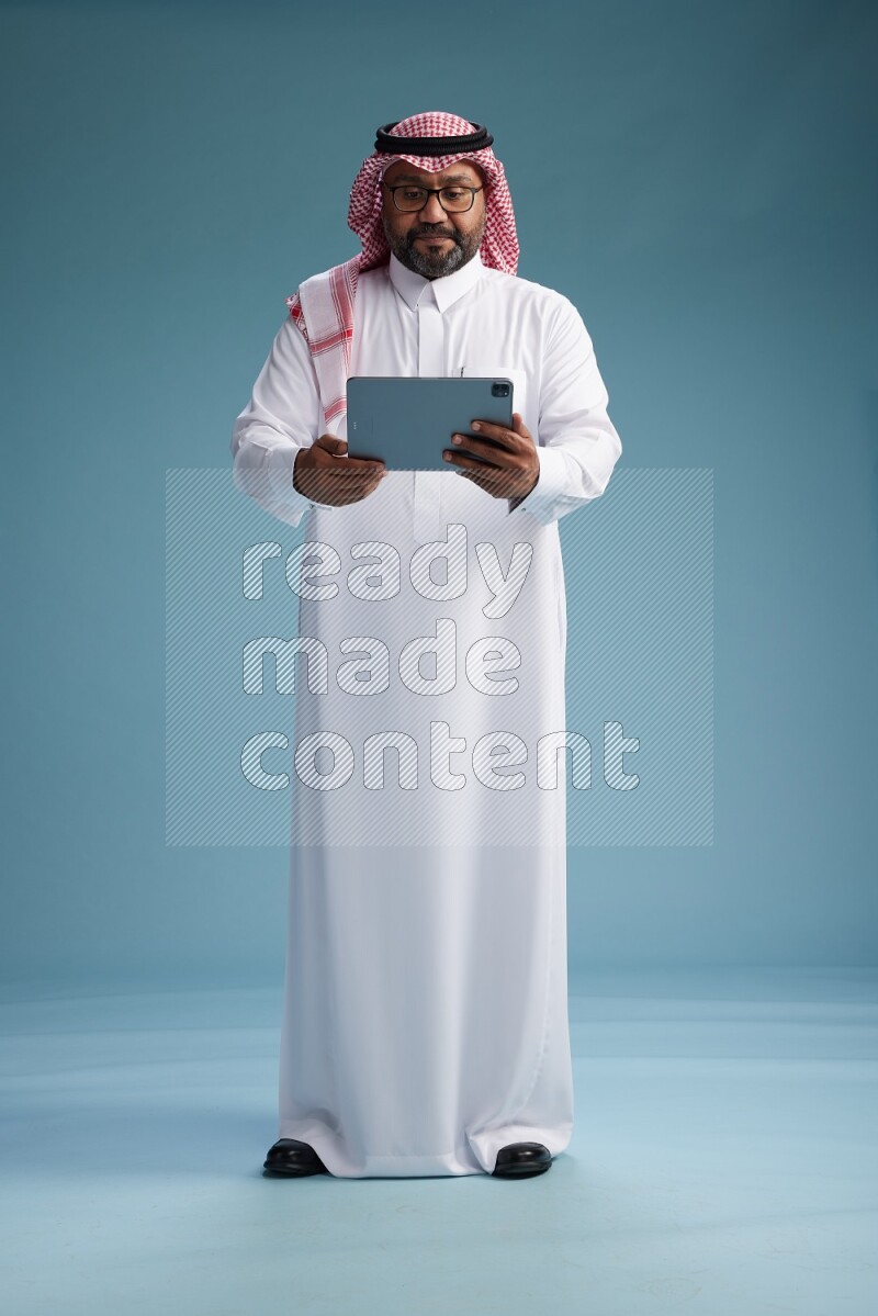 Saudi Man with shimag Standing holding a tablet on blue background