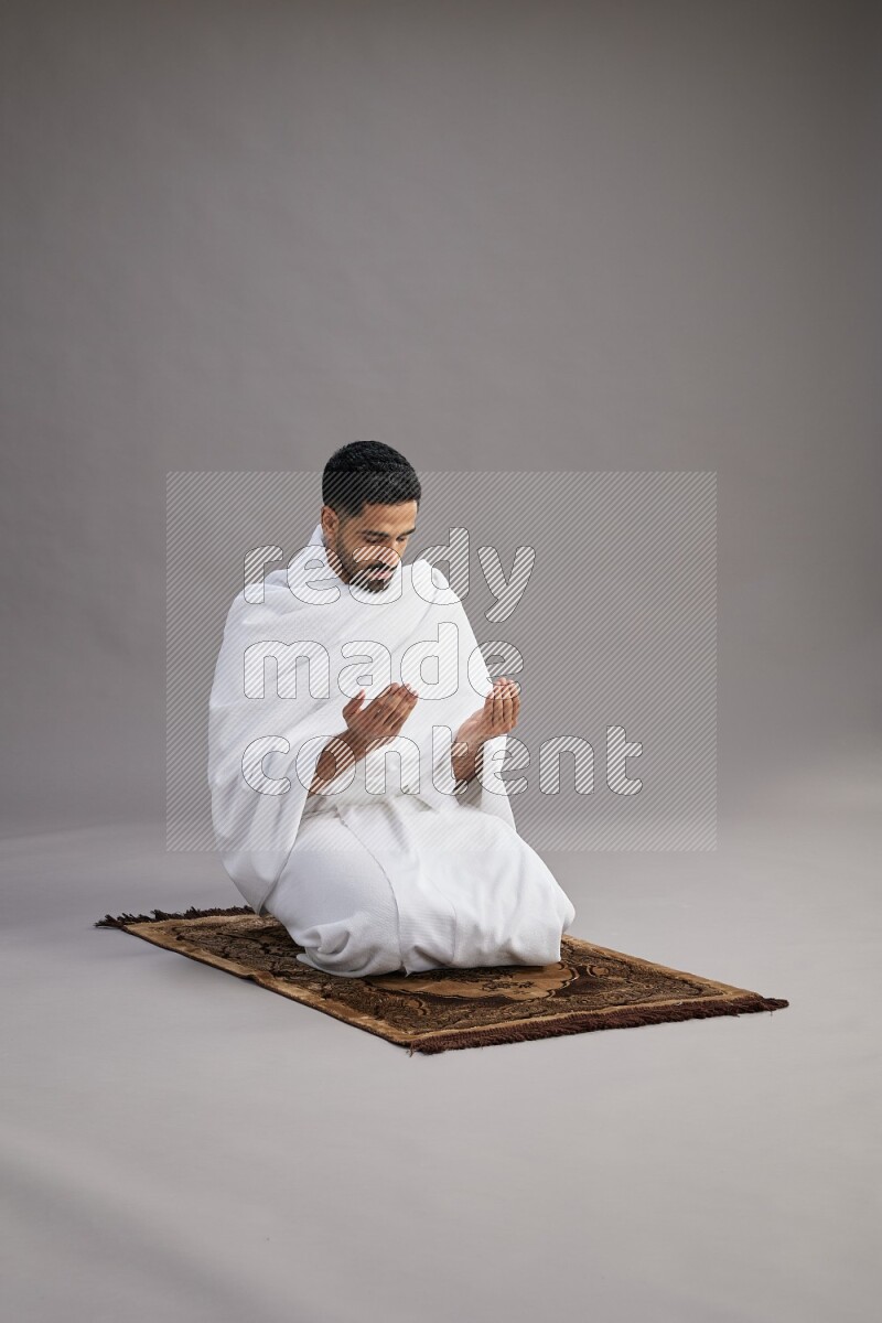 A man wearing Ehram performing dua'a on gray background