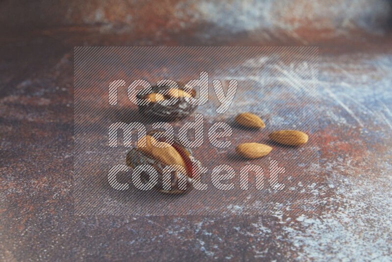two almond stuffed madjoul dates on a rustic reddish background