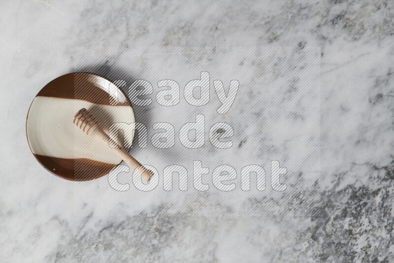 طبق فخاري متعدد الألوان مع ملعقة عسل خشبية بداخله على خلفية من الرخام الرمادي