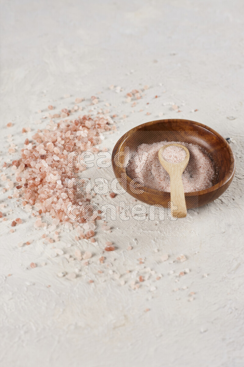 A pottery plate full of fine salt with bunch of coarse salt beside it on white background