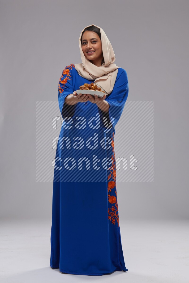 A Saudi woman standing wearing Jalabeya holding a plate of dates