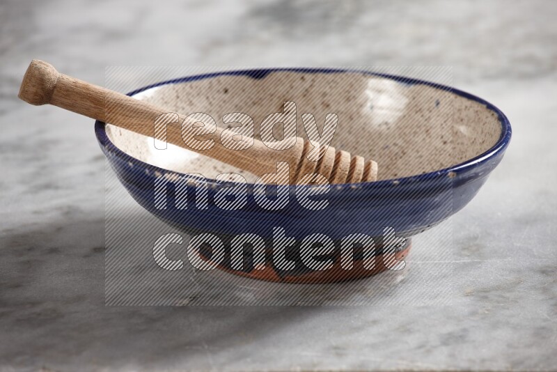 Multicolored pottery bowl with wooden honey dipper in it on grey marble background