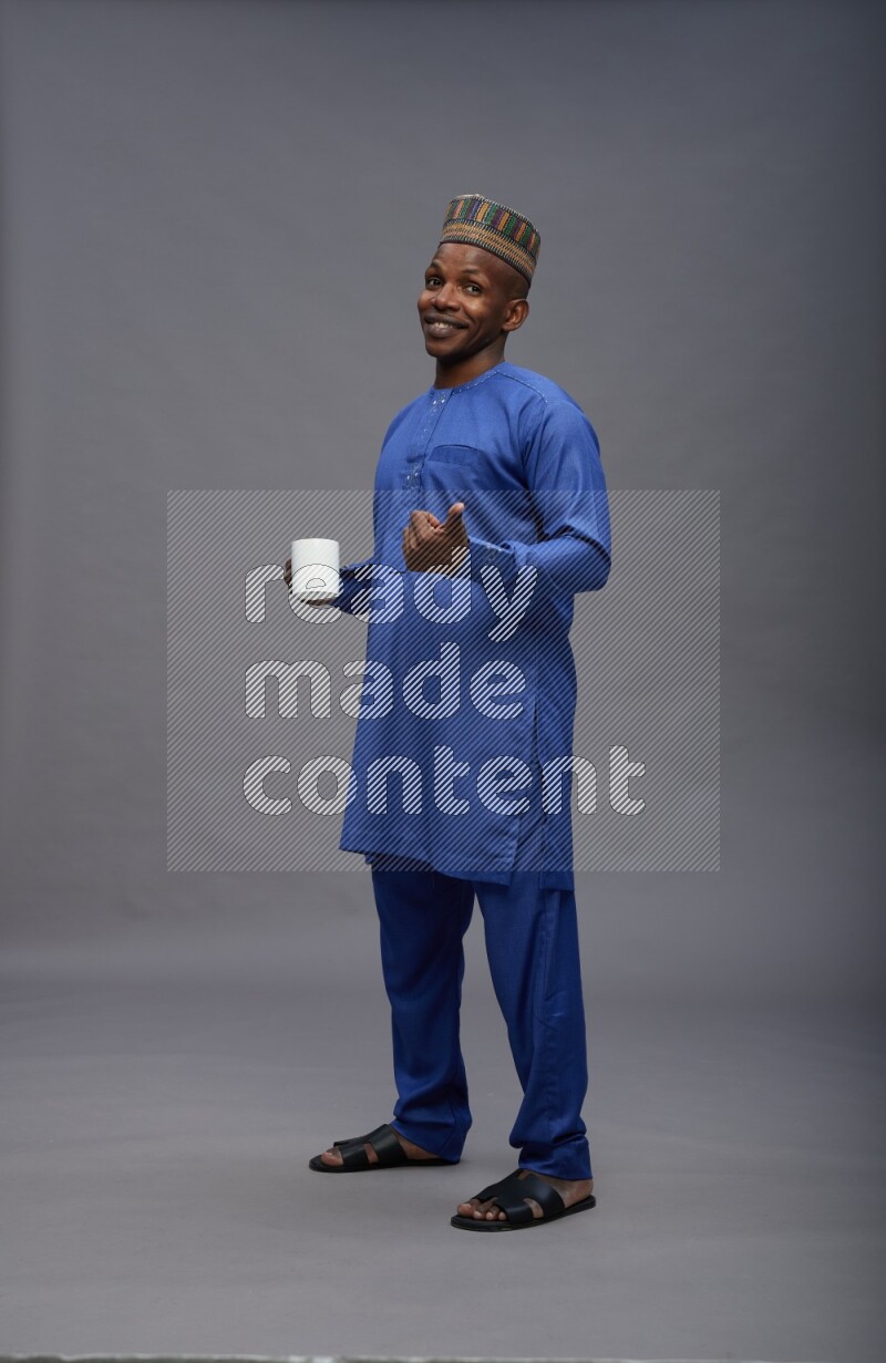 Man wearing Nigerian outfit standing holding mug on gray background
