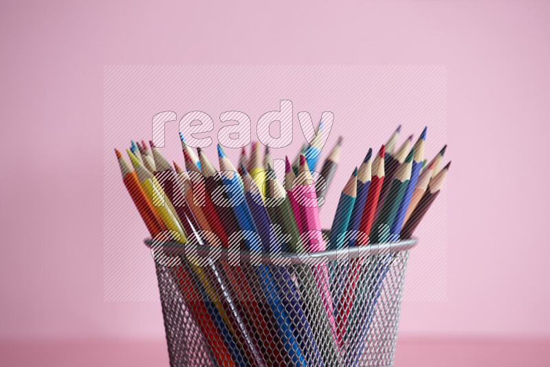 Pens, pencils and other different school supplies in a metal pen holder on rose background