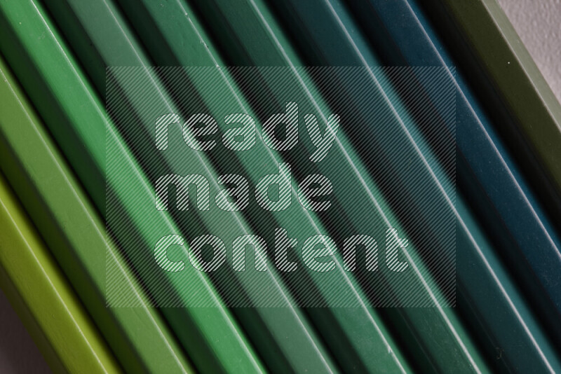 مجموعة من أقلام الرصاص الملونة مرتبة لتعرض تدرجا من الألوان الخضراء علي خلفية رمادية