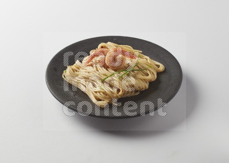 spaghetti pasta with white sauce on a black plate on a white background