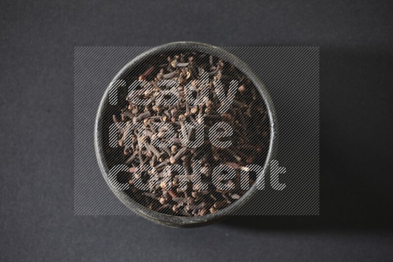 A black pottery bowl full of cloves on a black flooring