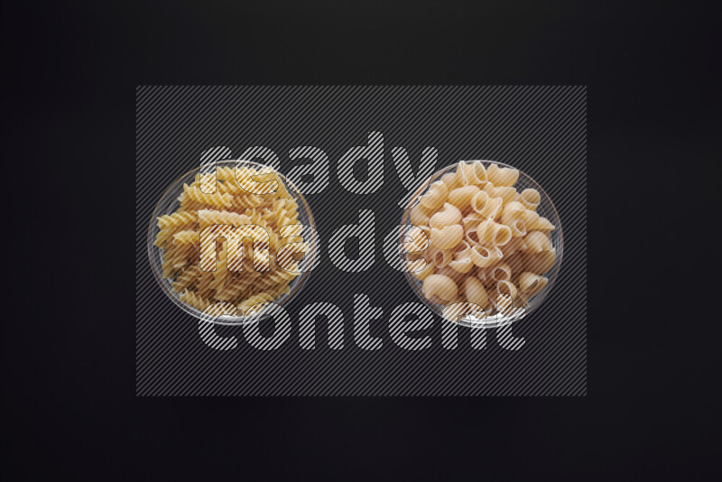 Different pasta types in glass bowls on black background