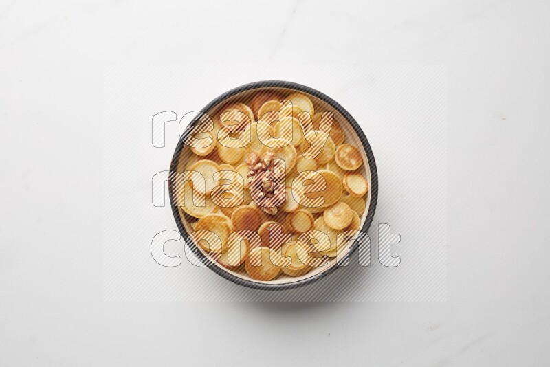 Top-view shot of walnut cereal pancakes in a round bowl on white background