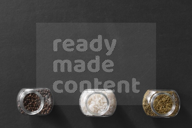 ملح والفلفل الأسود والكمون في أوعية زجاجية علي خلفية سوداء