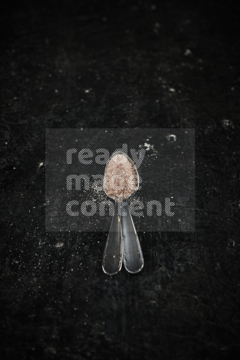 ملعقتان معدنيتان ممتلئتان بملح الهيمالايا الوردي على خلفية سوداء