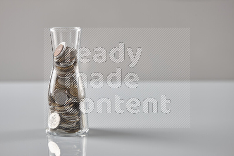 Random old coins in a glass jar on grey background