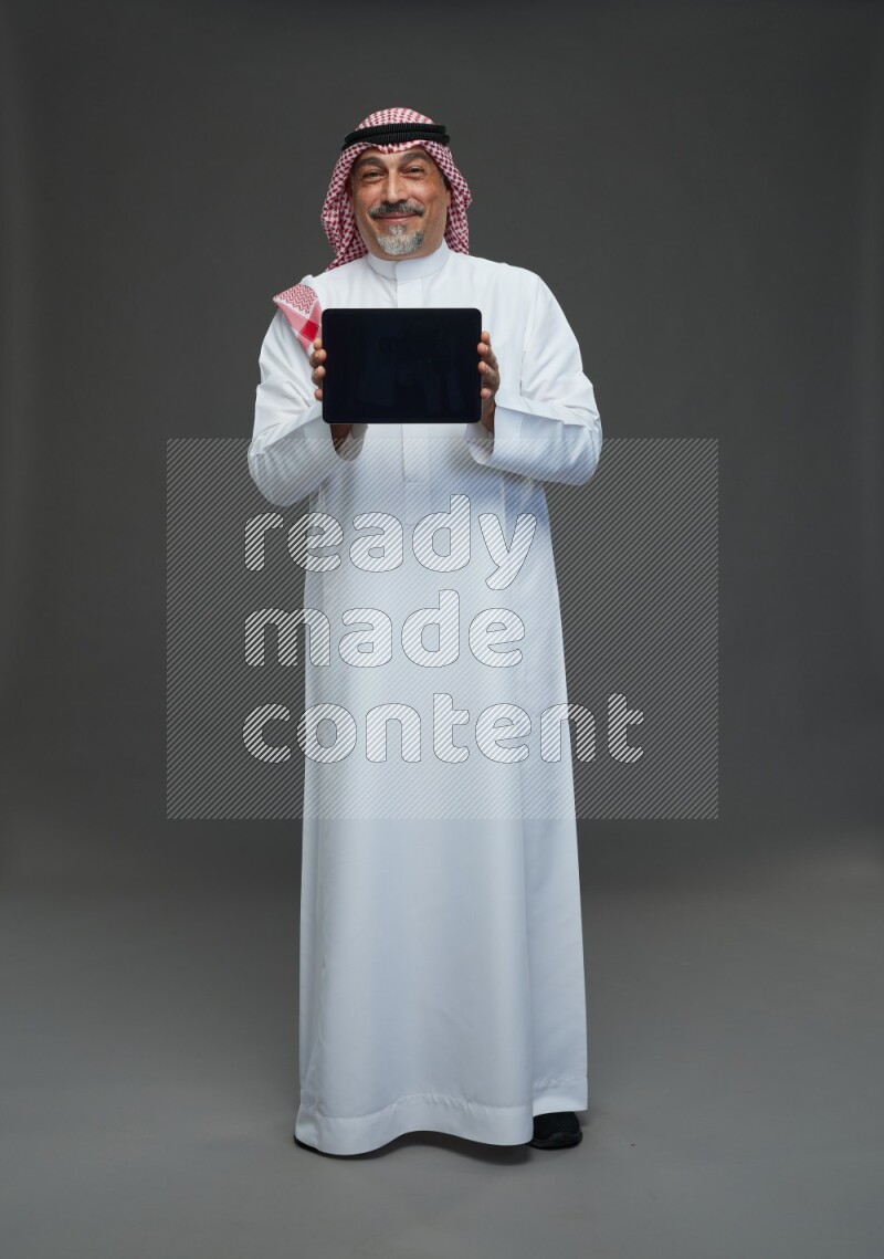Saudi man with shomag Standing working on tablet on gray background